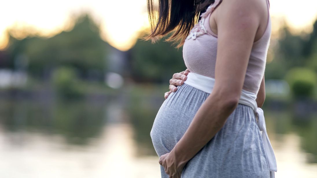 Pregnant woman stands outdoors feeling her bump