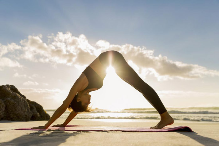 woman does downward dog yoga pose on a beach