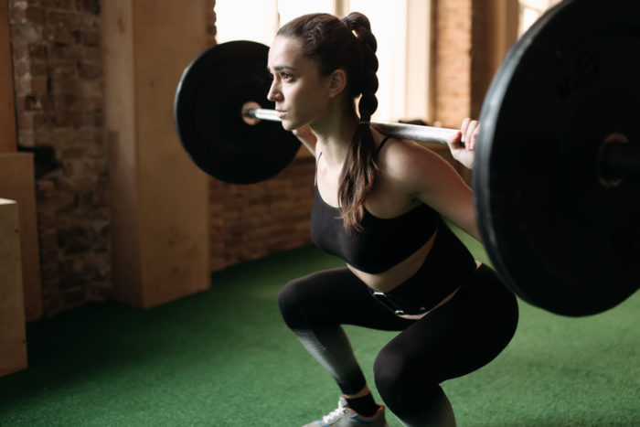 Woman doing a weighted squat in the gym as part of the essential lifts for women