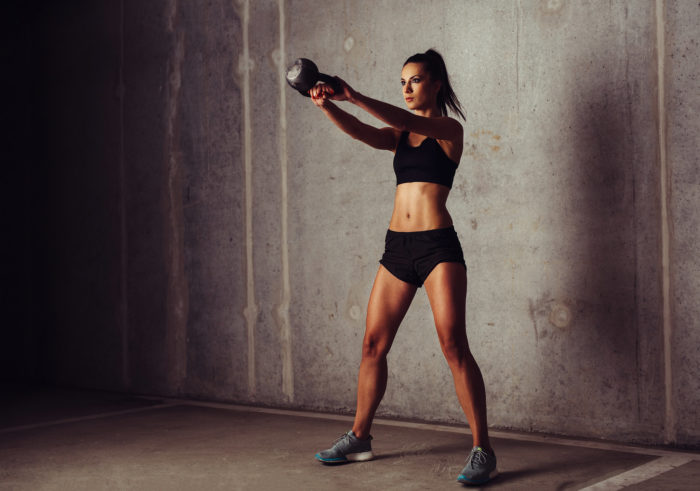 Woman performing at the top of a kettlebell swing during a HIIT leg workout 