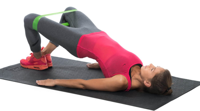 woman holding the top of a banded glute bridge