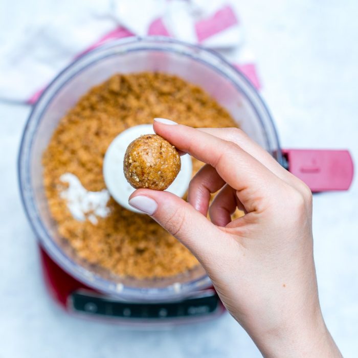 someone holding a peanut butter protein ball above a mixture of the ingredients