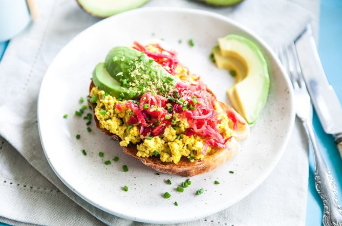 A plate with tofu, tomatoes and avocado on brown toast