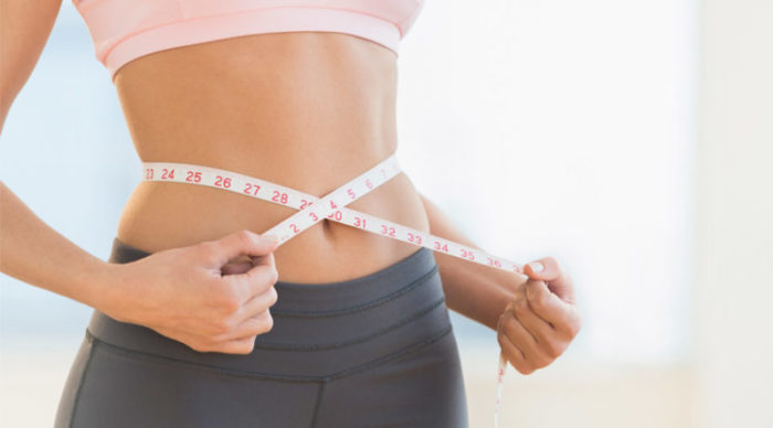 Woman with a measuring tape around her waist to indicate fat loss