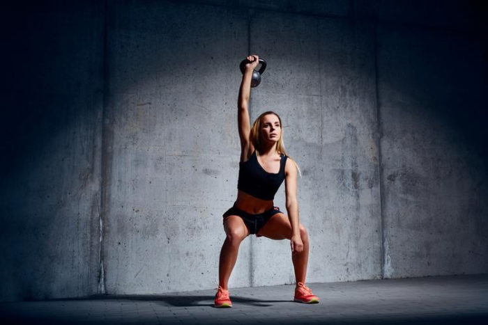 Woman at the top of a single arm kettlebell press in a fat loss kettlebell workout for beginners