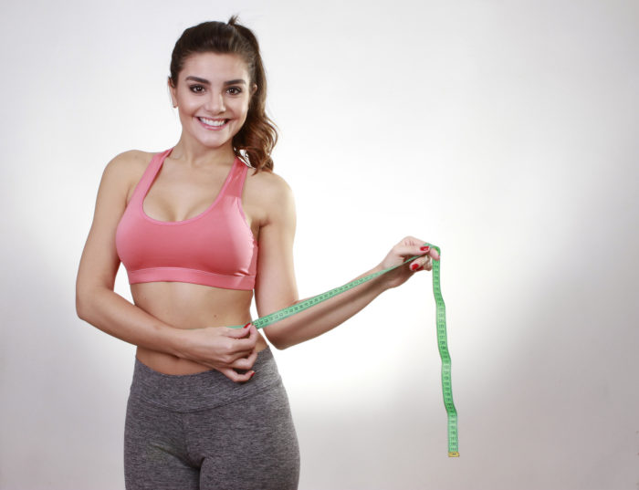 Woman showing fat loss with a measuring tape around her waist