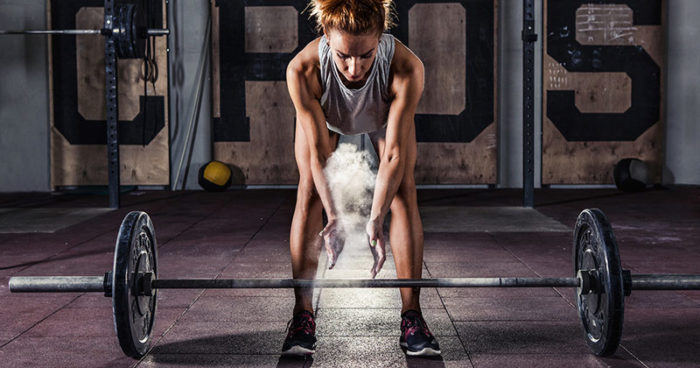 Woman chalking up her hands before she lifts the bar