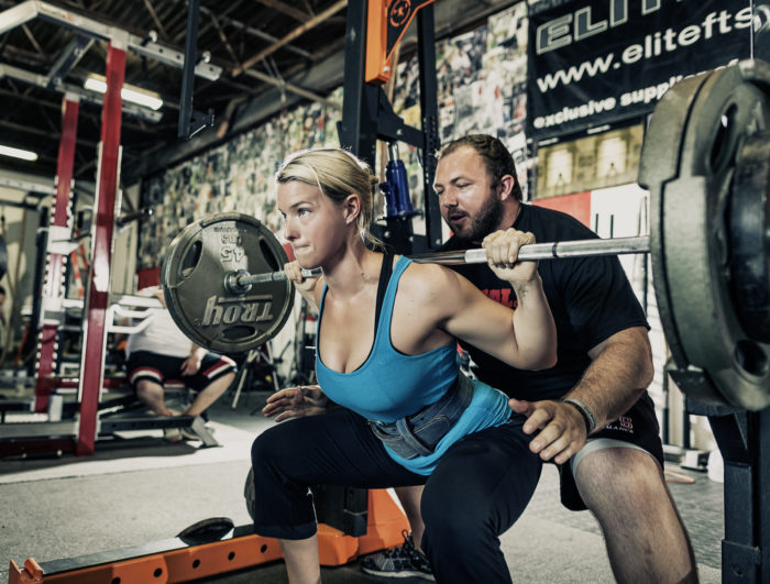 Woman at the bottom of a squat with a male spotter behind her